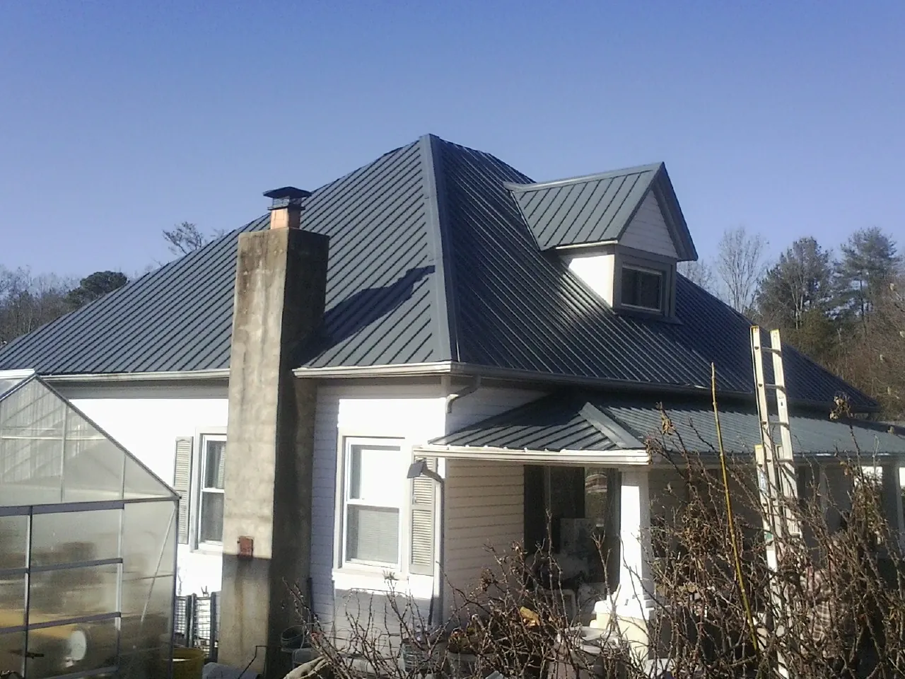 Dark blue standing seam metal roof on a white farmhouse with dormer — Slate & Tile Roof Repair by Roofing Brothers in Minford