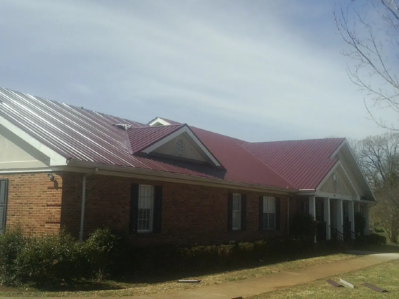 Red metal roof with gabled entries on a long brick building, from a Hail Damage Roof Repair job in Minford