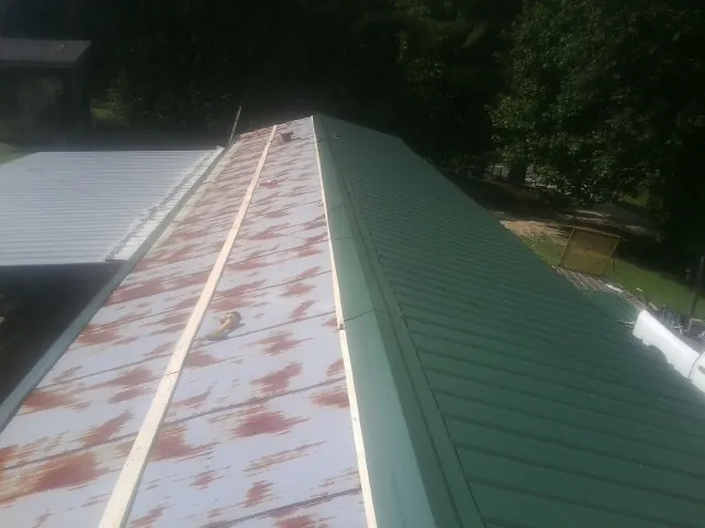 Old rusted panels beside newly installed green metal roofing — Wind Damage Roof Repair by Roofing Brothers in Minford