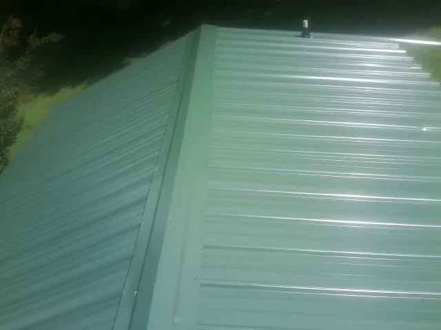 New green metal panels meeting at the ridge of a roof — Flat Roof Repair work by our crew in Minford