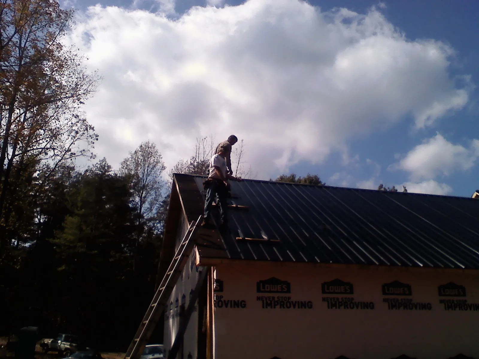Roofer fastening dark metal panels high against a cloudy sky, from a Roof Inspection job in Minford
