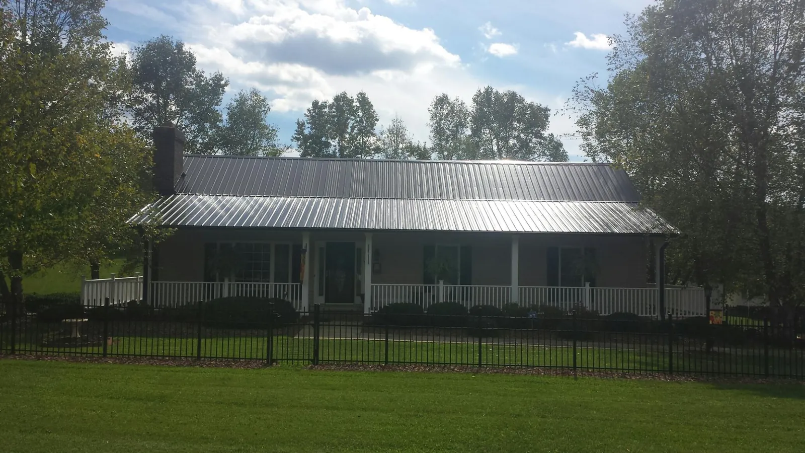 Gray metal roof on a brick ranch with a full width front porch — Gutter Guard Installation work by our crew in Minford