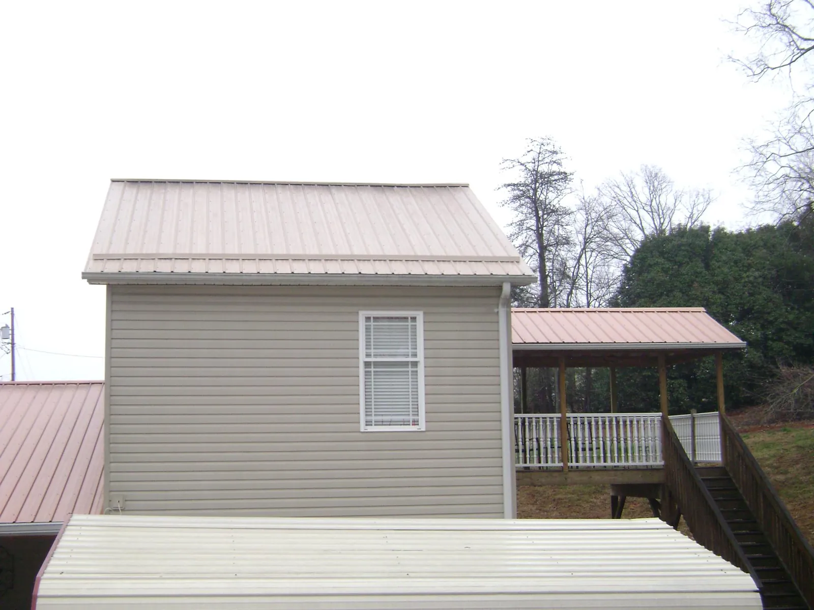Tan metal roofs on a two story addition and attached porch, from a Roof Replacement job in Minford